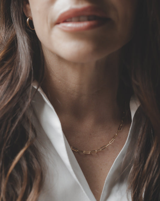 Close-up of a person wearing a white shirt and gold necklace with a neutral background