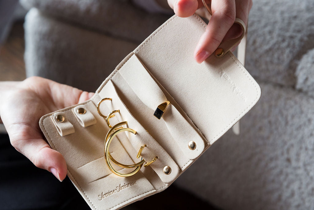 Beige jewelry case with gold rings held by a hand against a neutral background