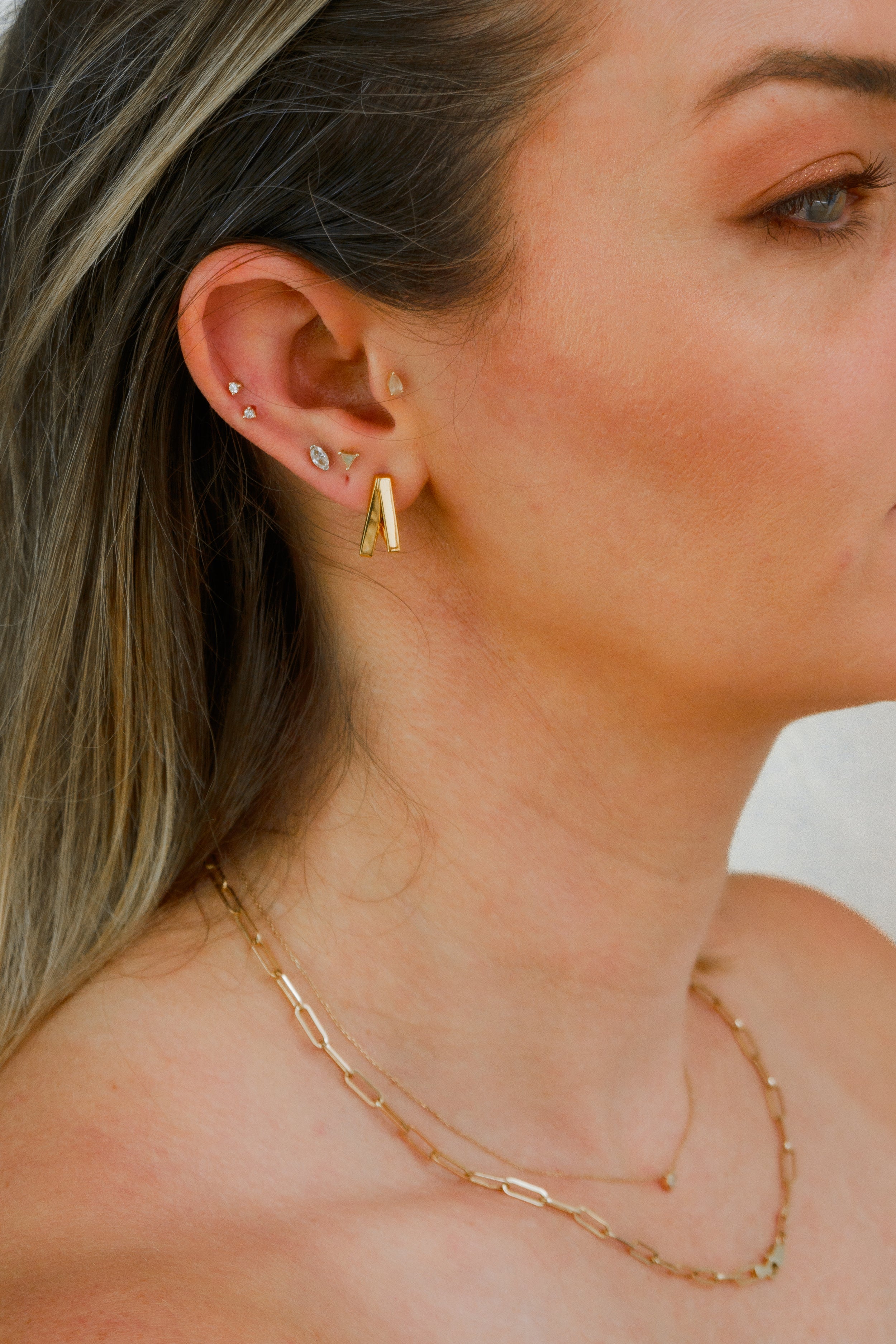 Woman wearing Armine + Ambrose The Namesake gold huggie earrings, close-up on a white background. 