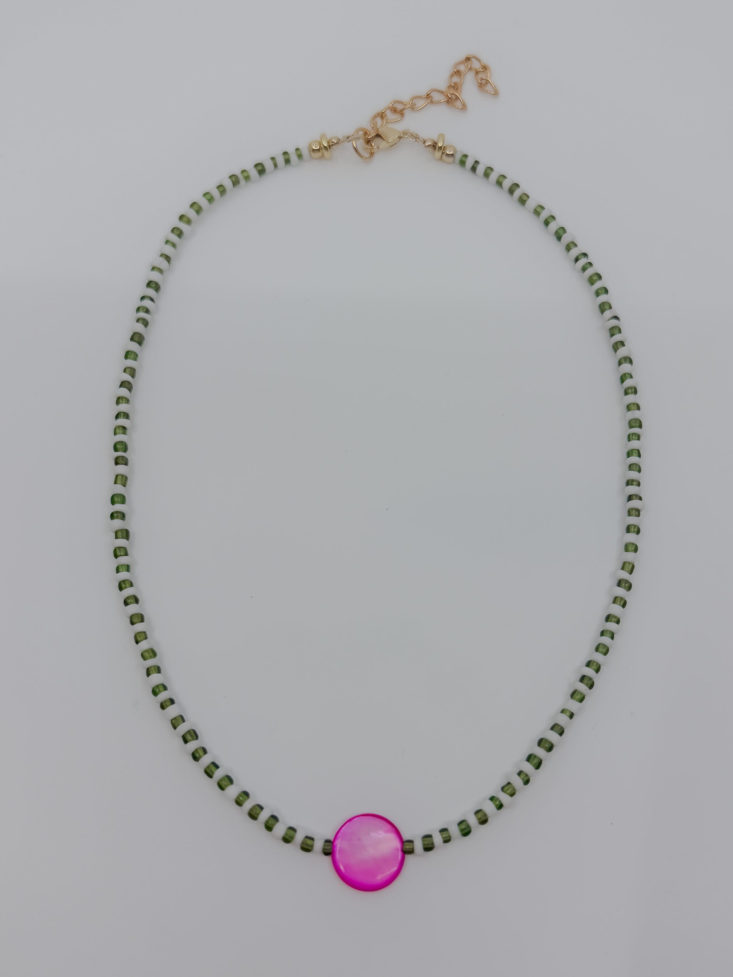 A beaded necklace featuring small green beads and a central, larger round pink mother of pearl pendant, with a gold-tone clasp and extender chain.