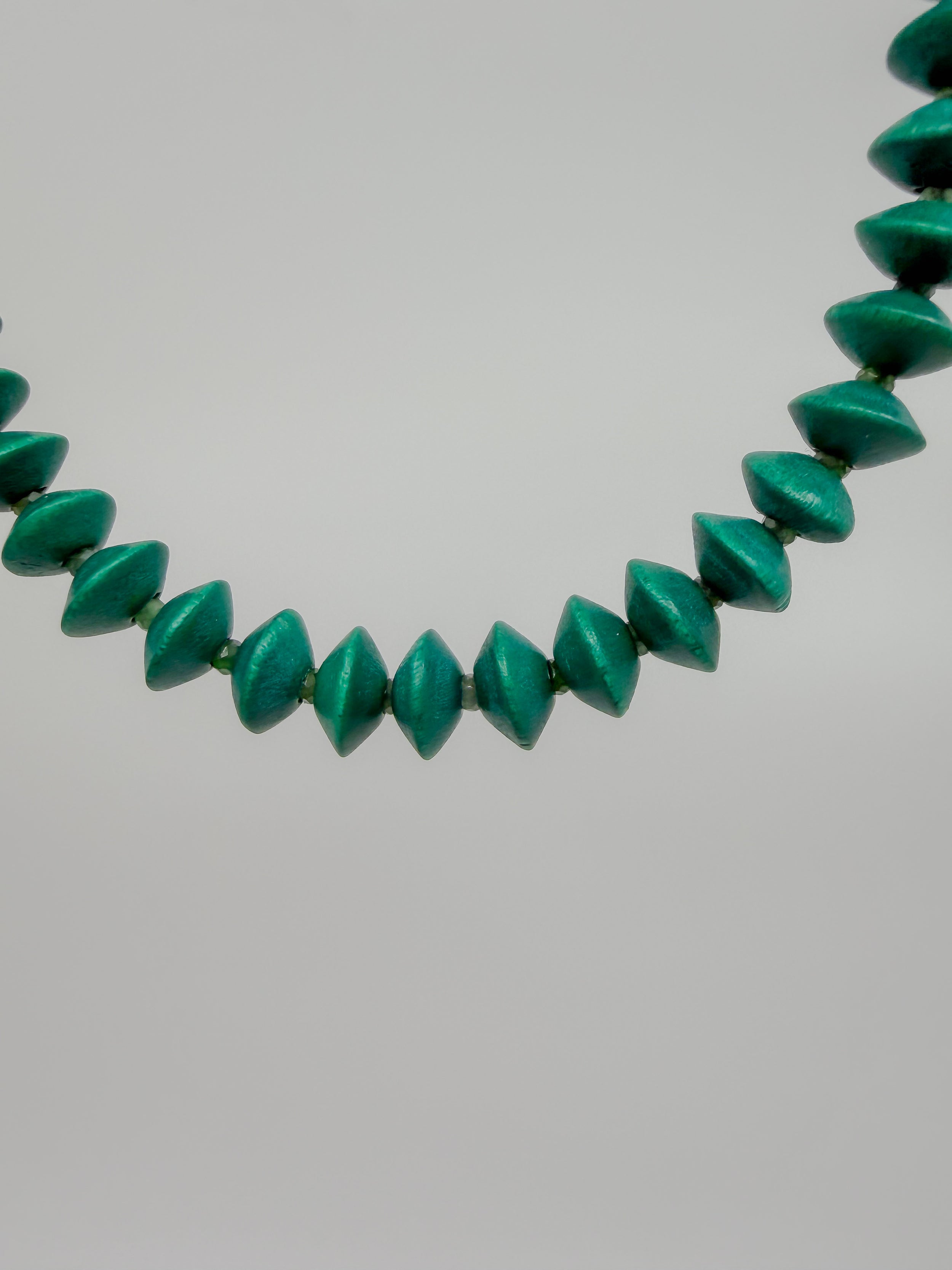 A close-up of a beaded bracelet featuring faceted, elongated beads in a vibrant emerald green color, set against a plain light gray background.