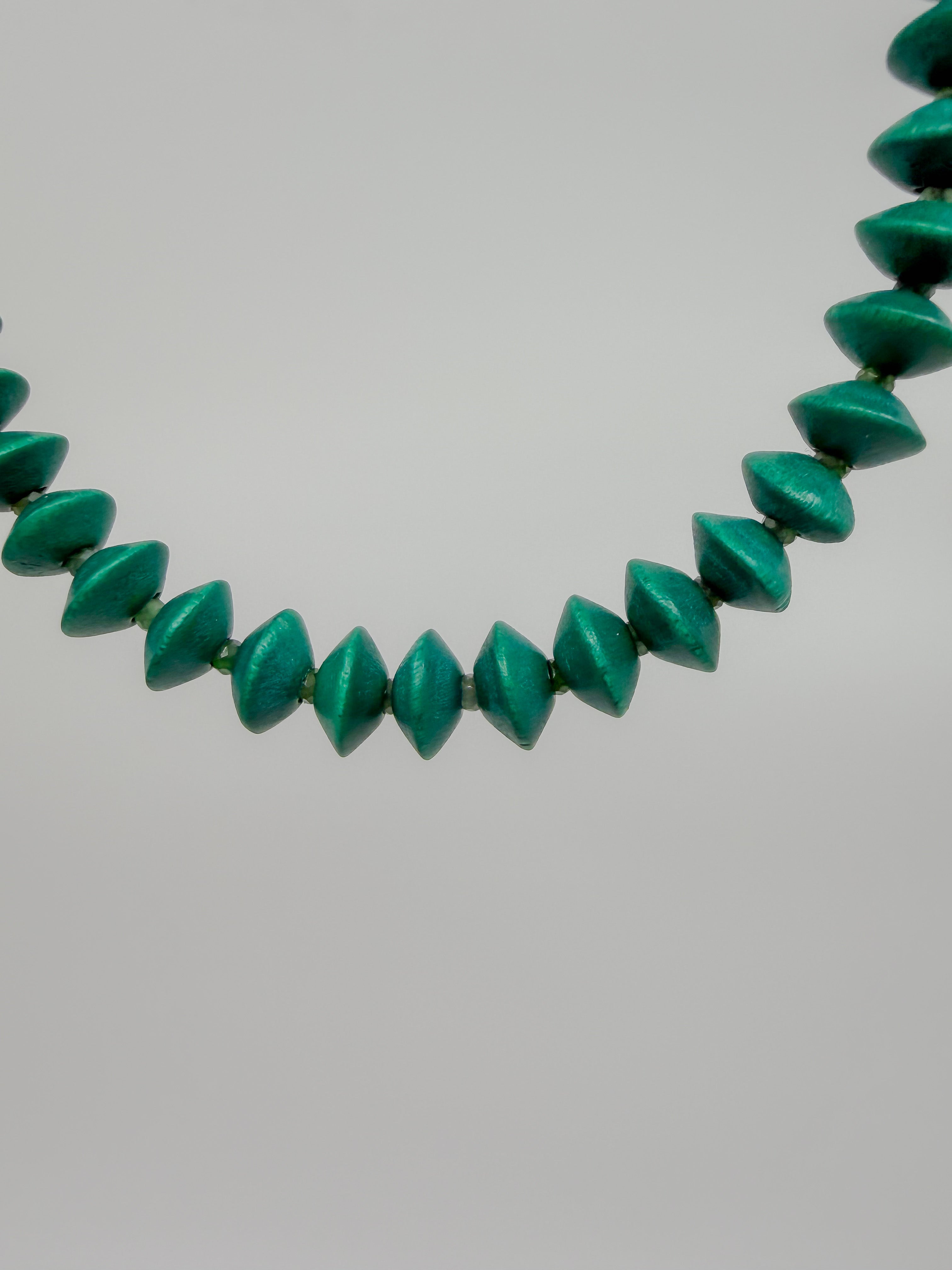 A close-up of a beaded bracelet featuring faceted, elongated beads in a vibrant emerald green color, set against a plain light gray background.