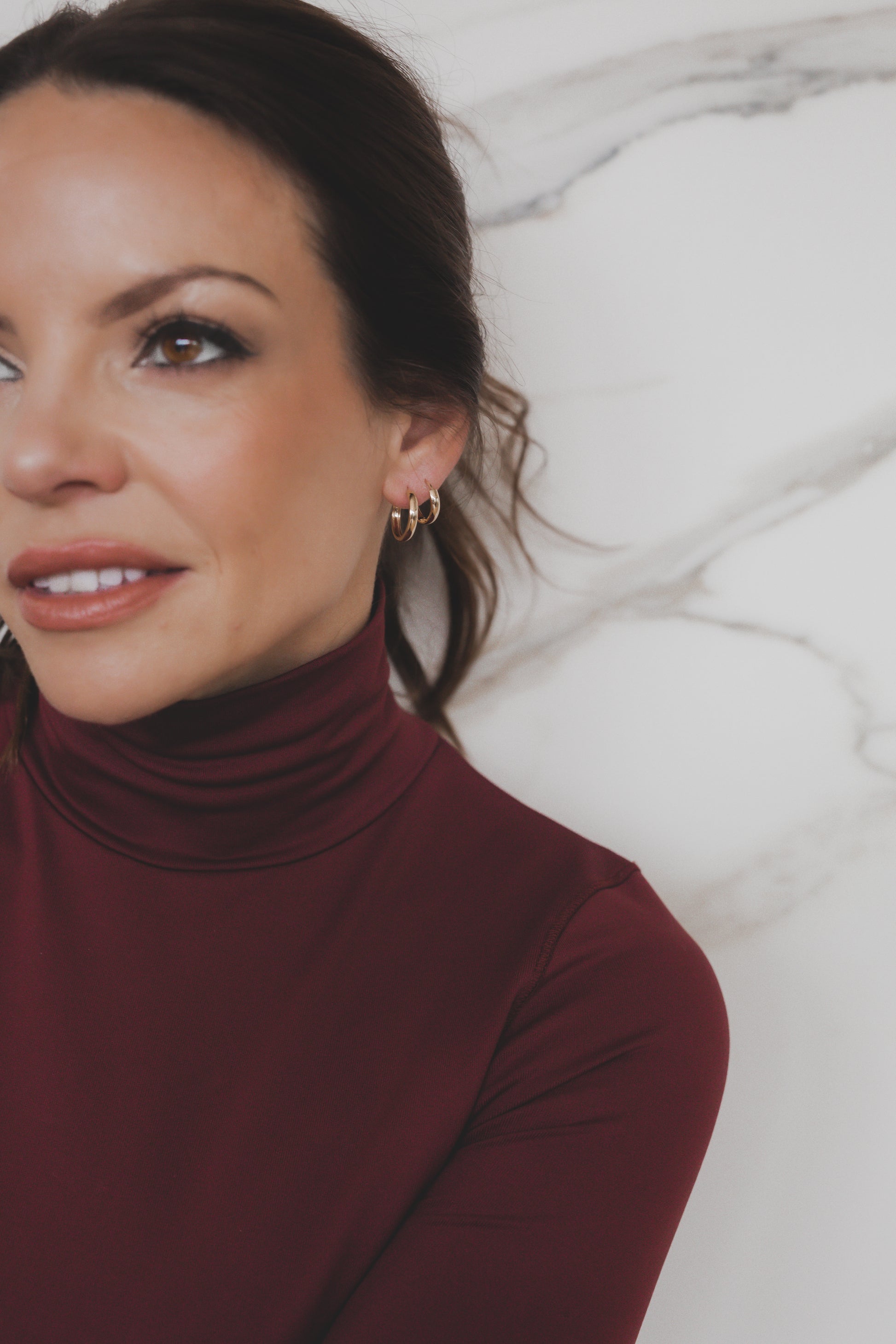 Woman wearing a burgundy turtleneck against a white marble background