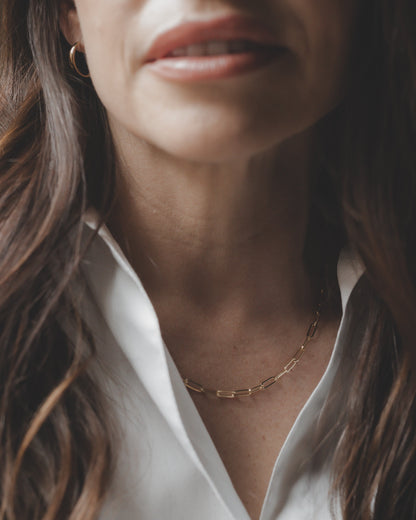 Close-up of a person wearing a white shirt and gold necklace with a neutral background