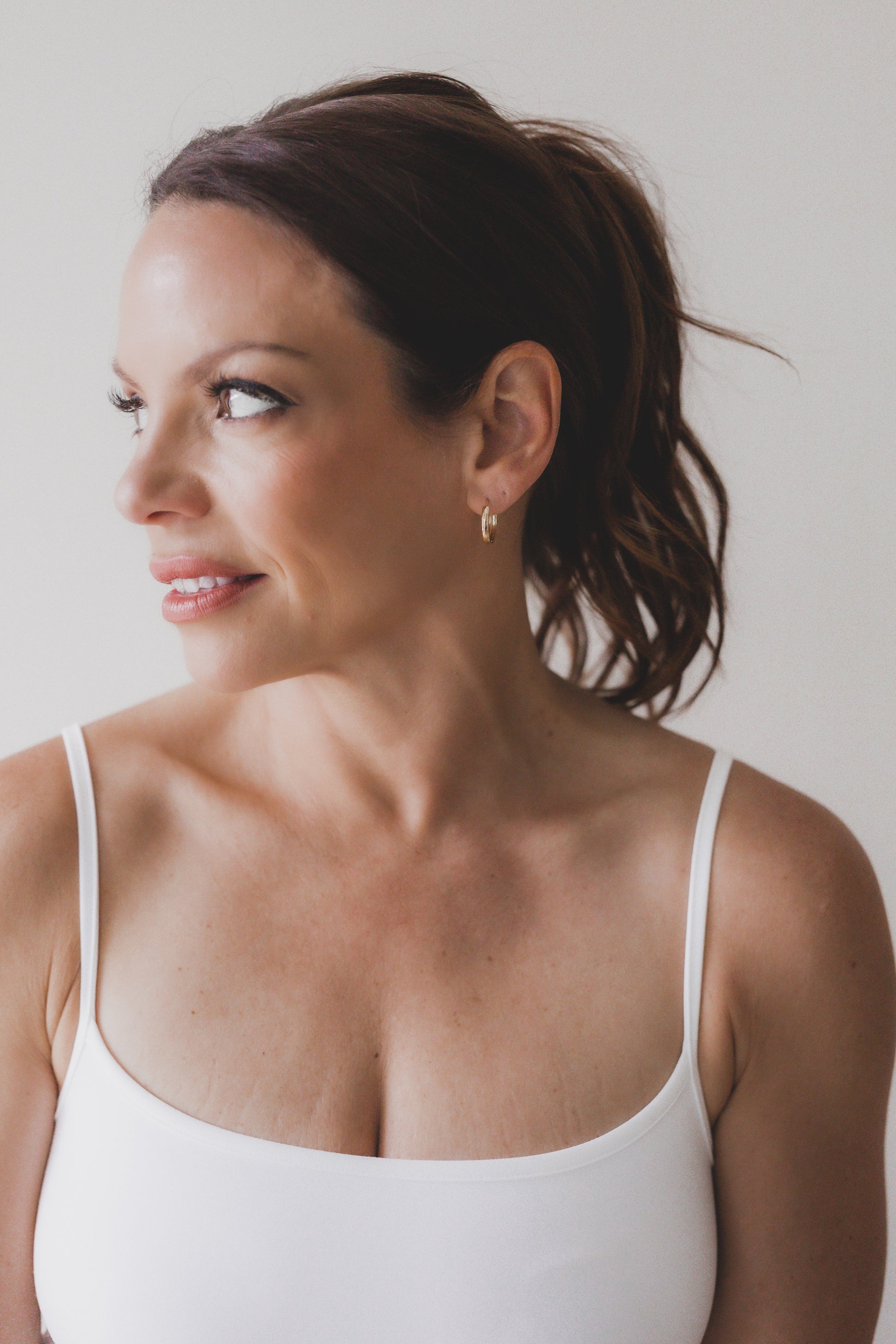 Woman wearing a white tank top against a plain background
