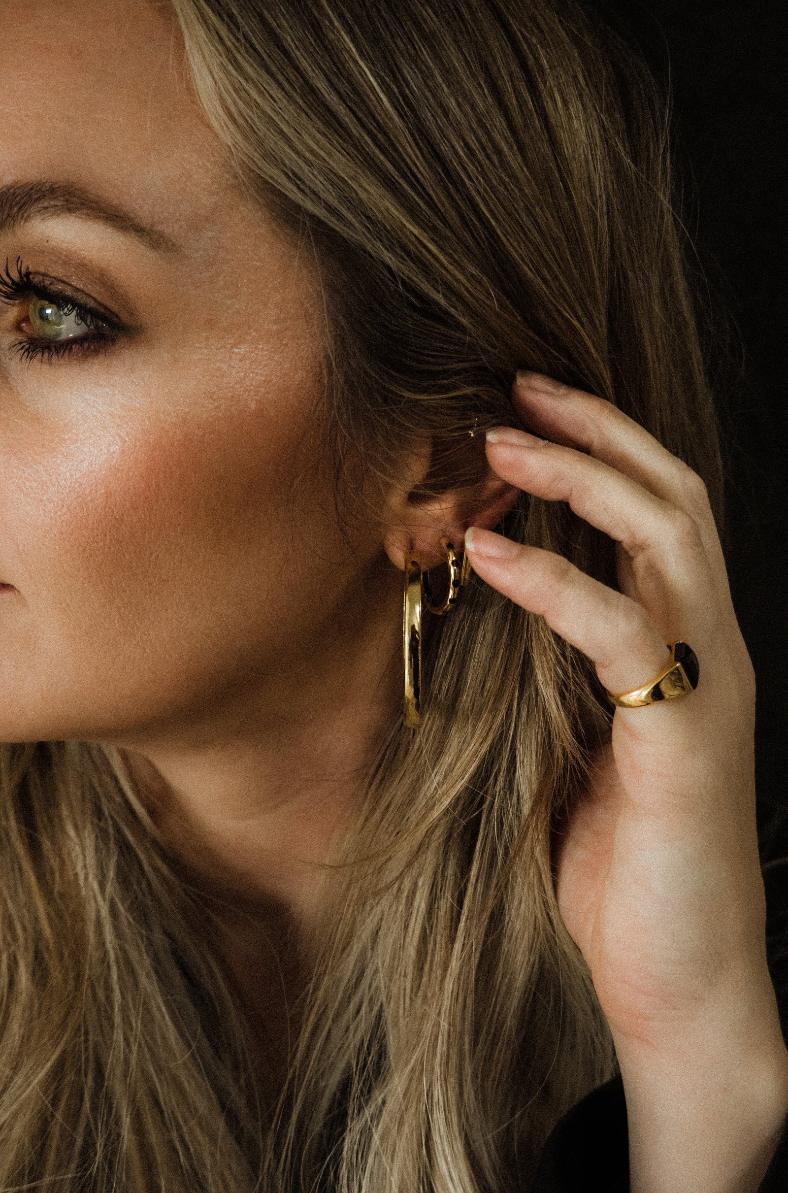 Woman wearing gold hoop earrings and a ring, with a close-up of her ear.