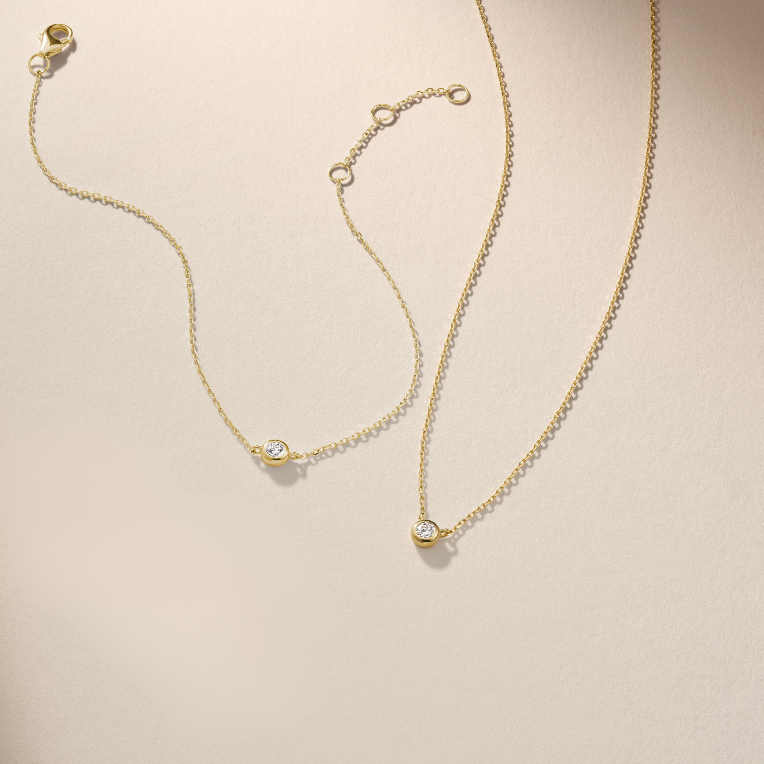 Armine + Ambrose Gold necklace and bracelet with small round diamond pendants on a beige background