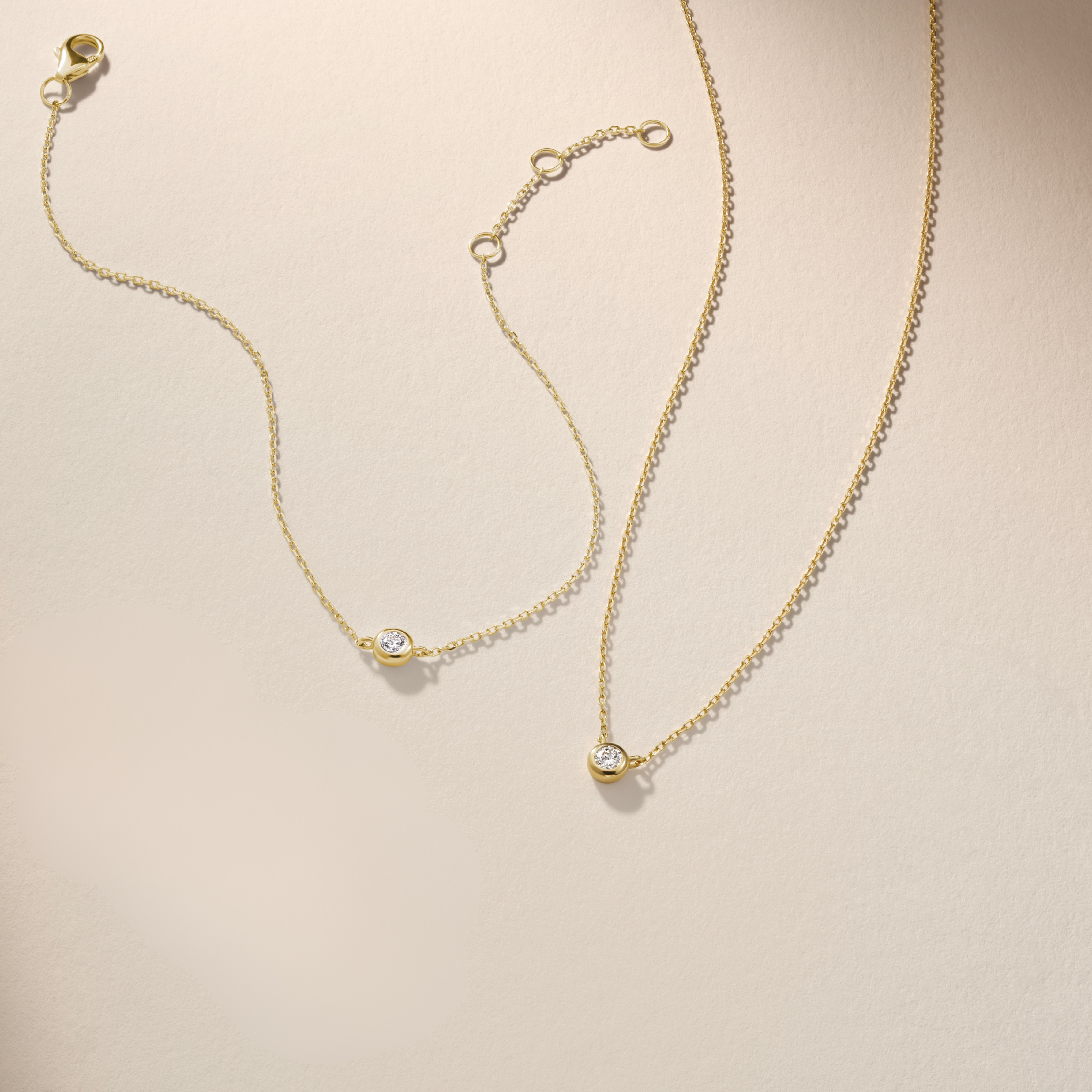 Armine + Ambrose Gold necklace and bracelet with small round diamond pendants on a beige background
