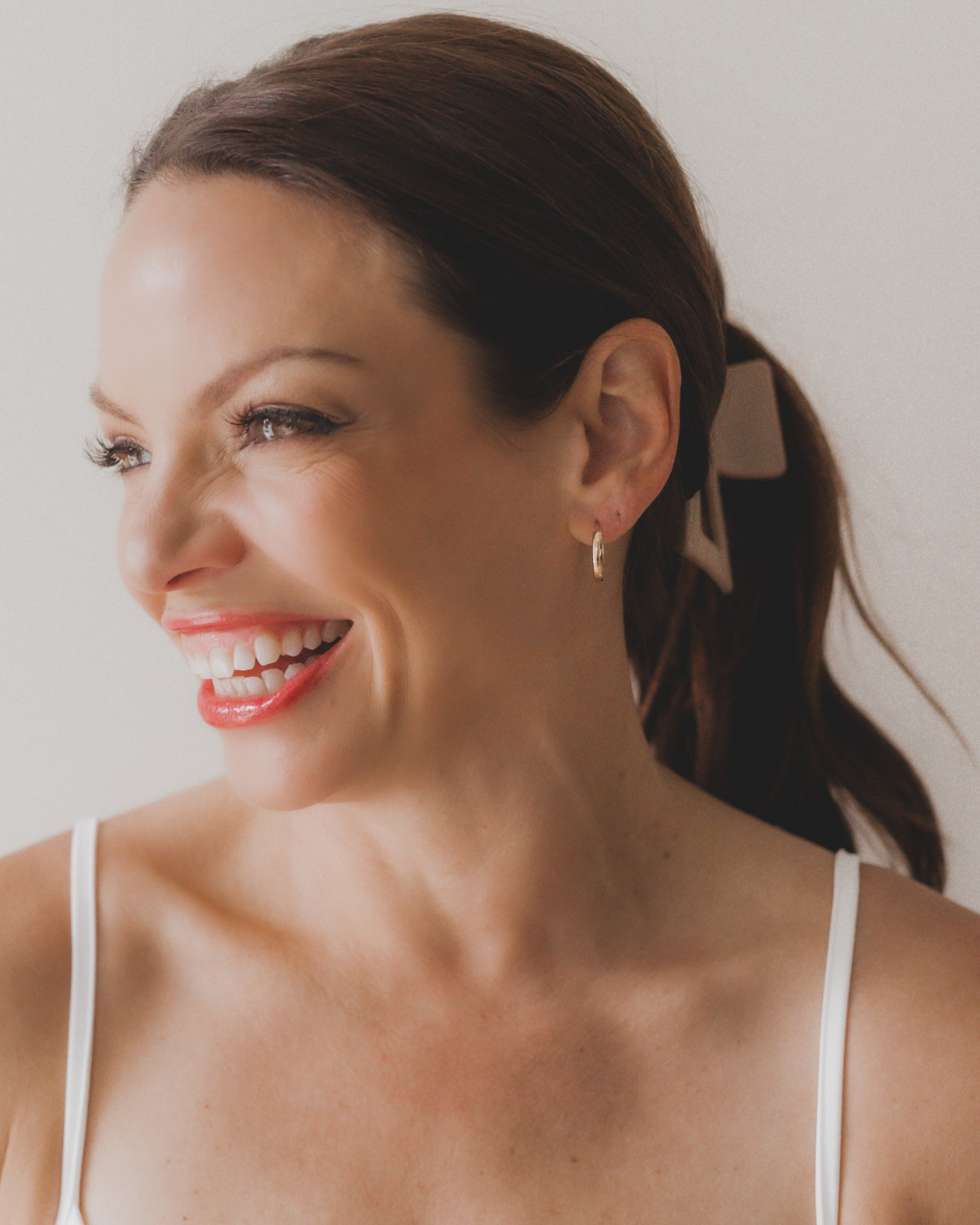 Woman with a ponytail wearing a white top against a plain background