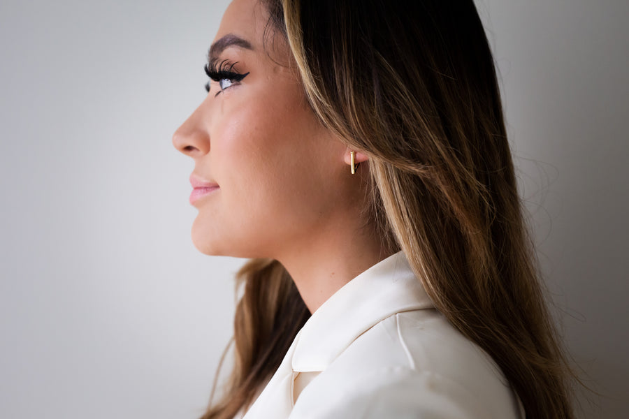 Model wearing Armine + Ambrose The A's inverted-A gold huggie earrings on a white background