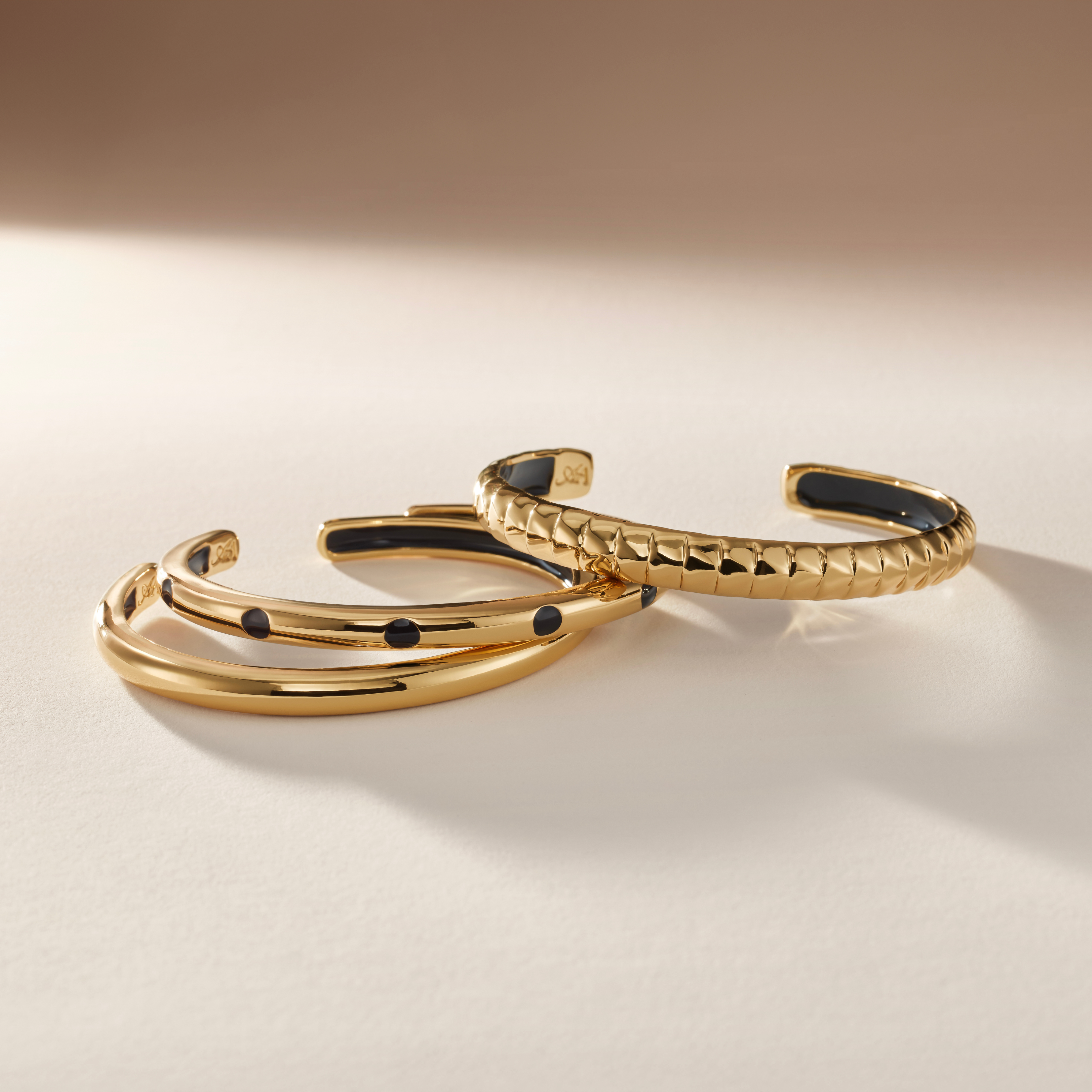 Three Gold bracelets with black accents on a beige background